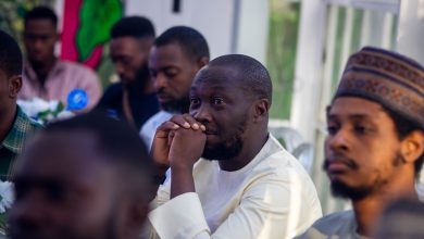 People seated at a gathering, with one person attentively listening, hands clasped near their face.