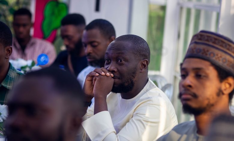 People seated at a gathering, with one person attentively listening, hands clasped near their face.