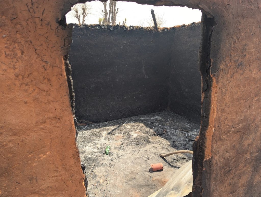 View through a window of a burnt and empty mud-walled room with debris on the floor.