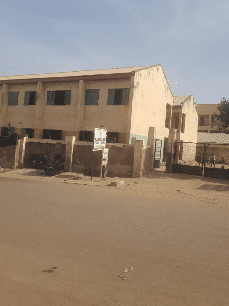 A two-story building with weathered walls on a sunny day, with a sign and a cart in front, located along a quiet street.