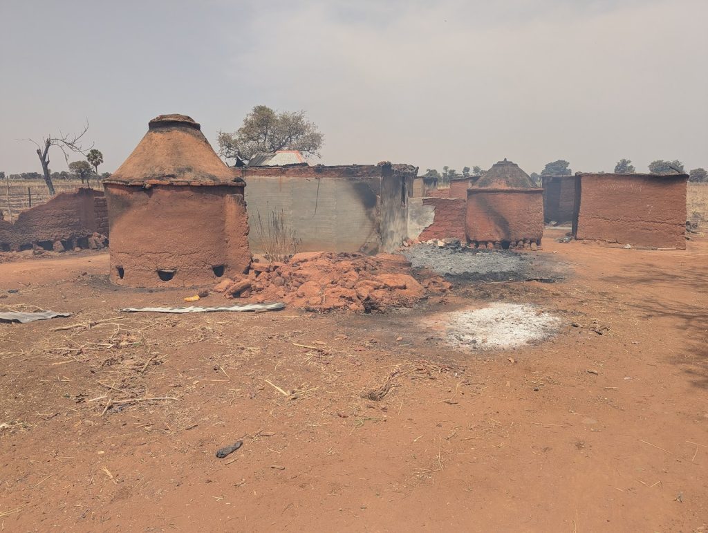 Rural scene with traditional clay kilns and burnt ground under a hazy sky. Sparse trees and dry earth in the background.