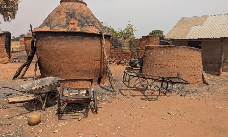 Large clay ovens with wooden supports, plus a wheelbarrow and cart in a sunlit rural setting.