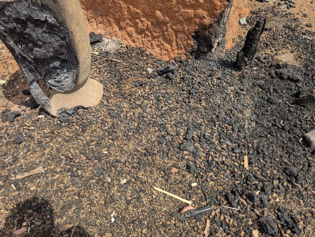 Charred tree trunks and scorched ground covered with small rocks and ash.
