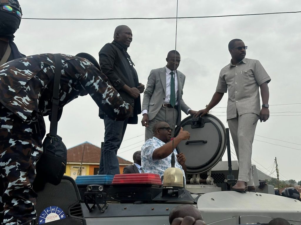 A group of men, including one in camouflage, stand and talk on top of an armored vehicle on a cloudy day.