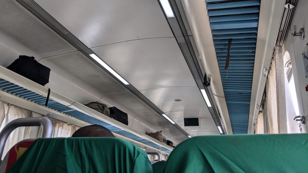 Interior view of a train carriage, showing overhead luggage racks and green seat covers.