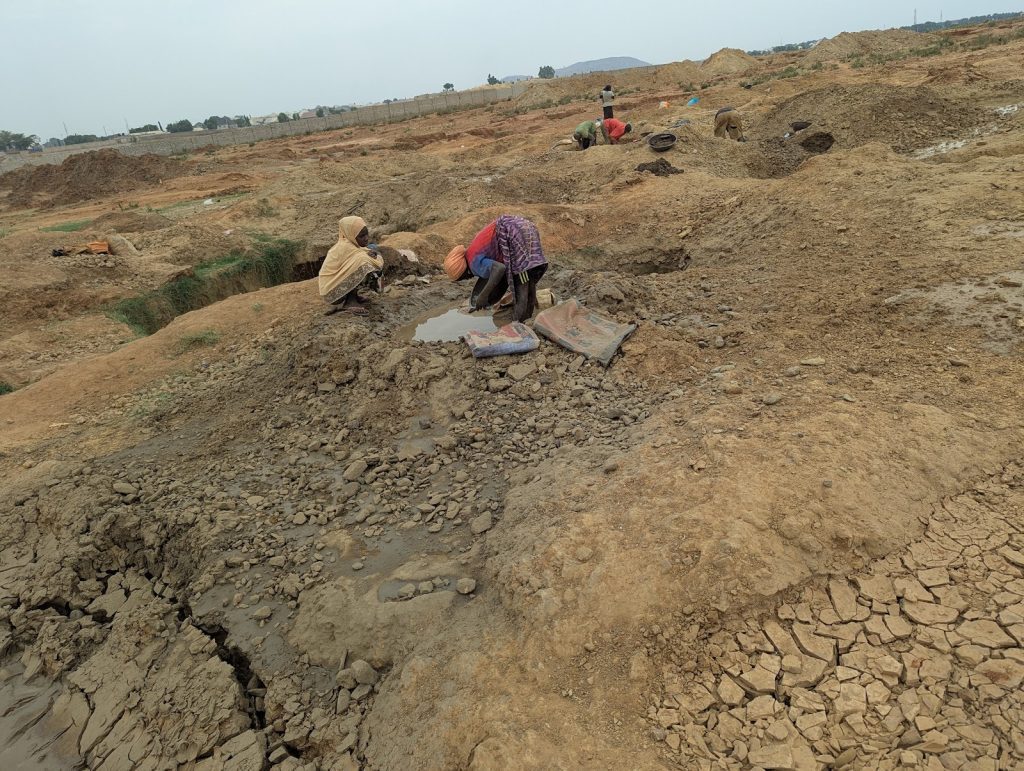 People digging in a dry, barren landscape with small pools of water.