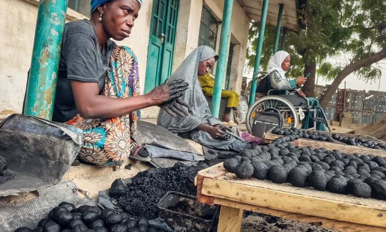 People forming coal balls by hand, sitting outdoors. One person in a wheelchair, another in colorful attire, surrounded by trays of coal balls.