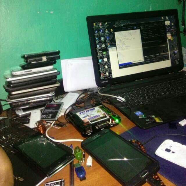 Cluttered desk with a laptop, many phones, and various tech gadgets. A software program is open on the laptop screen.