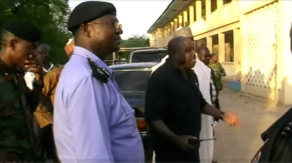 A group of people, some in uniform, stand outside a building engaged in conversation during daylight.
