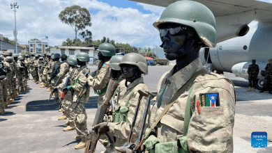 Soldiers in camouflage uniforms and helmets stand in formation near a military aircraft, with a South Sudan patch visible on a uniform.