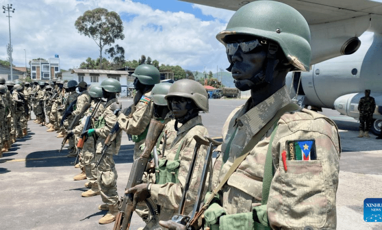 Soldiers in camouflage uniforms and helmets stand in formation near a military aircraft, with a South Sudan patch visible on a uniform.