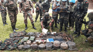 Soldiers in camouflage and UN helmets examine items laid out on the ground, discussing and taking notes.