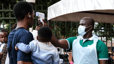 A person having their temperature checked with an infrared thermometer by a masked healthcare worker. A child is held by the person.