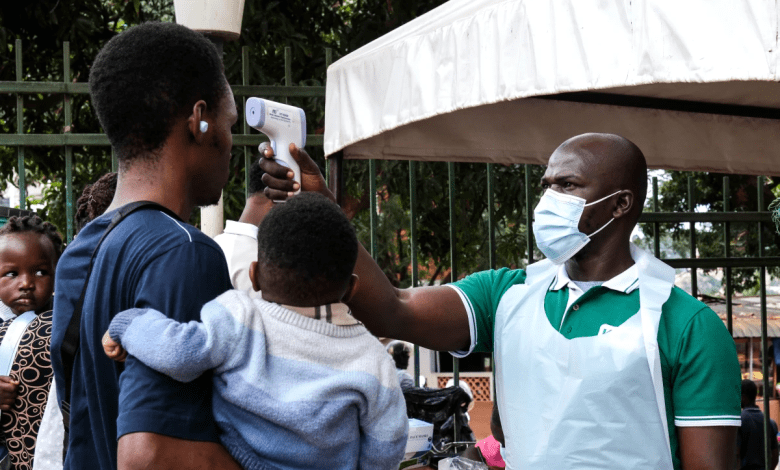 A person having their temperature checked with an infrared thermometer by a masked healthcare worker. A child is held by the person.