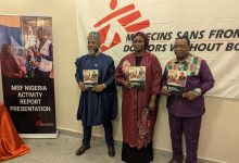 Three people stand holding MSF Nigeria activity reports in front of a banner. A sign reads "MSF Nigeria Activity Report Presentation."