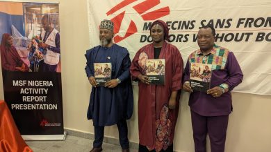 Three people stand holding MSF Nigeria activity reports in front of a banner. A sign reads "MSF Nigeria Activity Report Presentation."