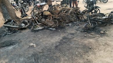 Burned motorcycle frames on the ground with people and intact bikes in the background.