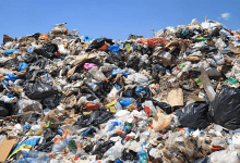 A large pile of assorted trash and plastic bags at a landfill under a clear blue sky.