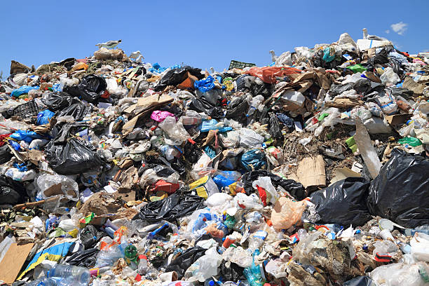 A large pile of assorted trash and plastic bags at a landfill under a clear blue sky.