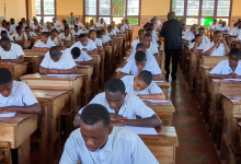 Students in uniforms sitting in rows at wooden desks, focused on taking an exam in a classroom setting.