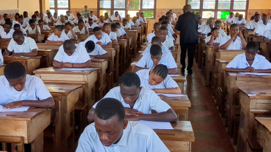 Students in uniforms sitting in rows at wooden desks, focused on taking an exam in a classroom setting.