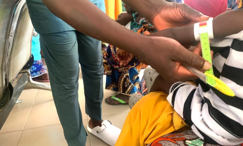 Healthcare worker measuring a child's arm circumference with a tape for nutritional assessment.