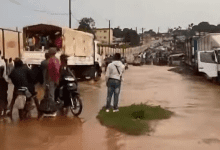 Flooded street with trucks, motorbike, and people navigating through water.