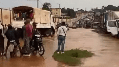 Flooded street with trucks, motorbike, and people navigating through water.