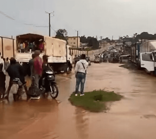 Flooded street with trucks, motorbike, and people navigating through water.