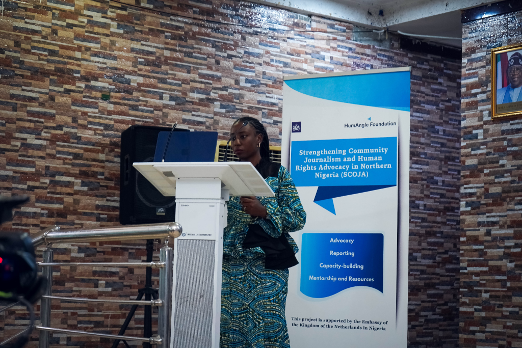 A woman speaks at a podium next to a banner about strengthening journalism and human rights advocacy in Northern Nigeria.