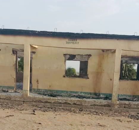An abandoned, partially burnt building with missing windows and a damaged roof, surrounded by a barren landscape.