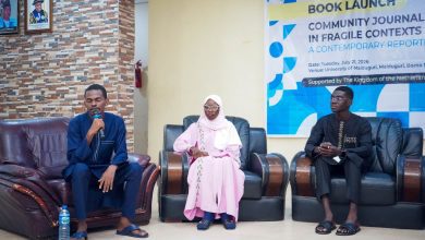 Three people seated on chairs at a book launch event, one speaking into a microphone.