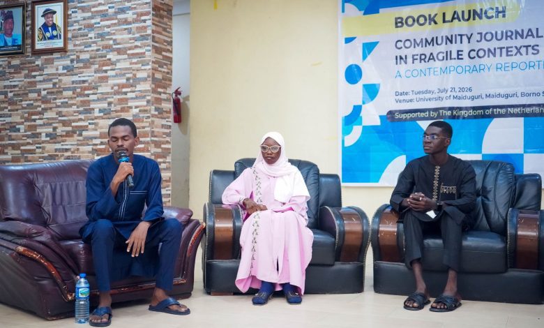 Three people seated on chairs at a book launch event, one speaking into a microphone.