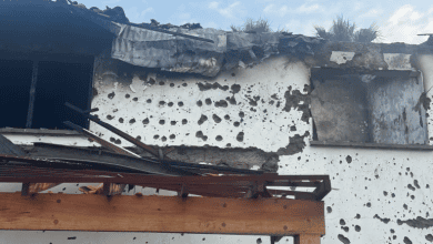 Damaged building with exterior walls covered in holes and debris from roof, under a partly cloudy sky.