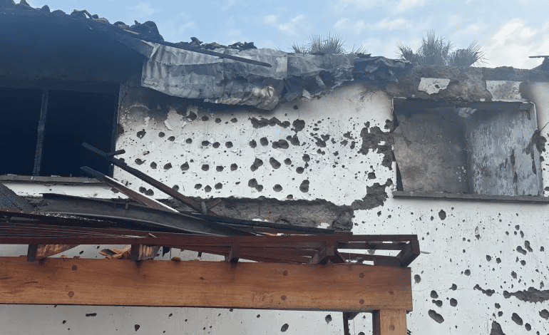 Damaged building with exterior walls covered in holes and debris from roof, under a partly cloudy sky.