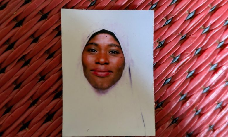 A portrait photo of a person in a light-colored headscarf on a red woven surface.