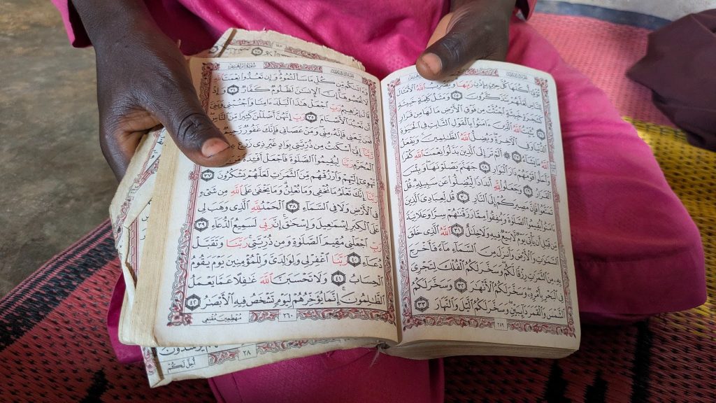 Person holding an open book with Arabic text, wearing pink clothing.